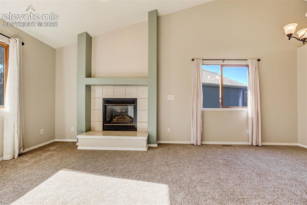 Image 6 of 50: Vaulted ceilings, a tile-surround fireplace with a hearth, and warm neutral