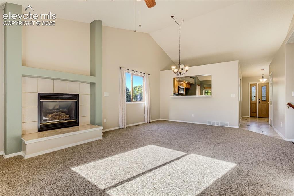 Image 7 of 50: Vaulted ceiling living space featuring a tiled fireplace, ceiling fan, and 