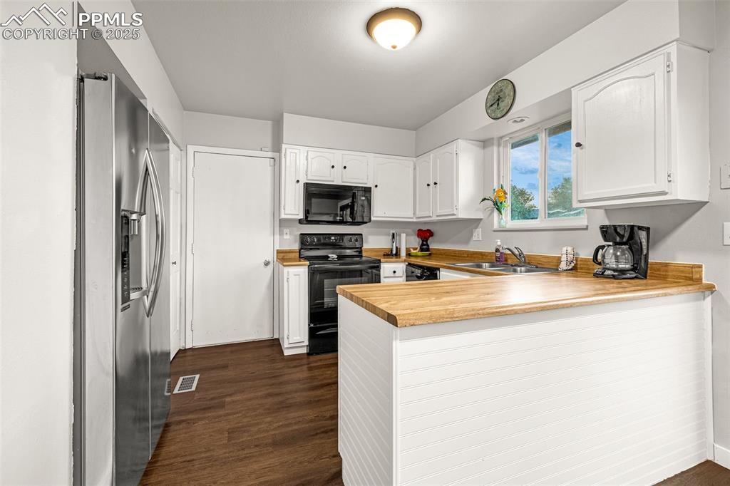 Image 10 of 22: Kitchen with a peninsula, white cabinetry, black appliances, and dark wood-