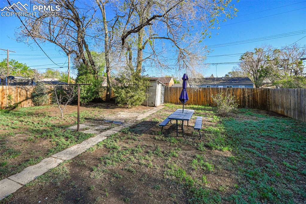 Image 26 of 28: Fenced backyard with a storage unit and an outbuilding