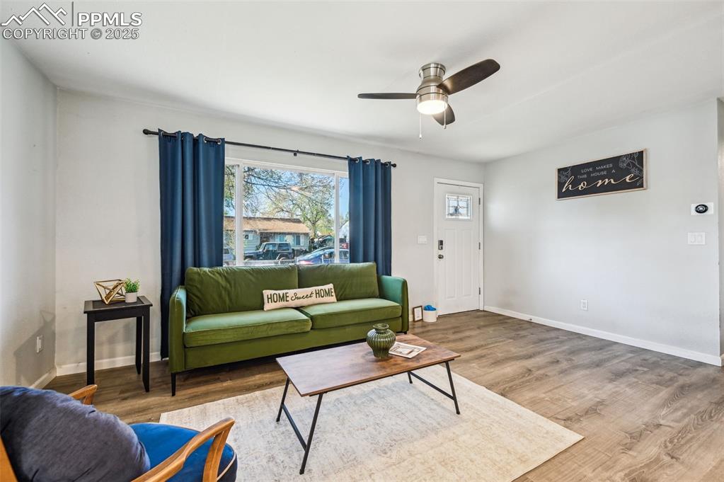 Image 7 of 28: Living room featuring a ceiling fan, wood finished floors, and baseboards