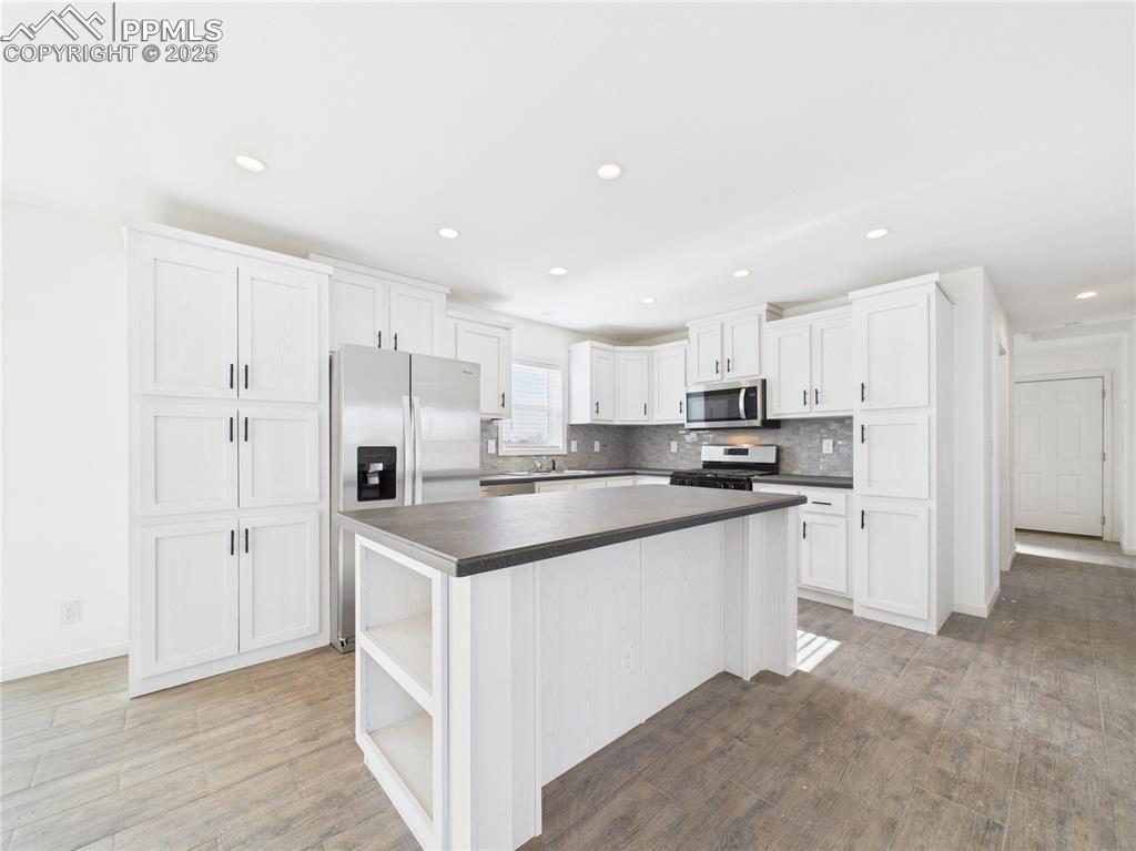 Image 12 of 50: Kitchen with white cabinets, stainless steel appliances, dark countertops, 