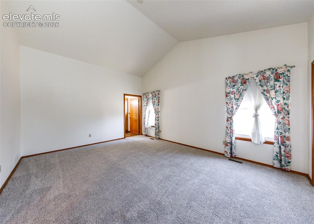 Image 12 of 22: Vaulted ceiling with white paint, light gray carpet, and wood trim