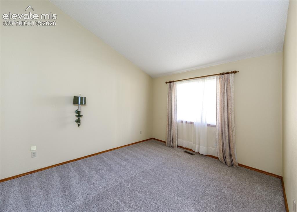 Image 14 of 22: Vaulted ceiling, wall-mounted sconce, light-toned walls, window with trim,