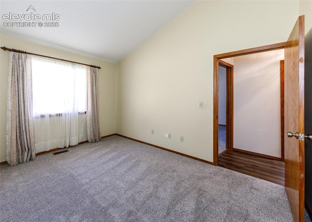 Image 15 of 22: Vaulted ceiling, wall-to-wall carpeting, wood-trim window with drapes, and