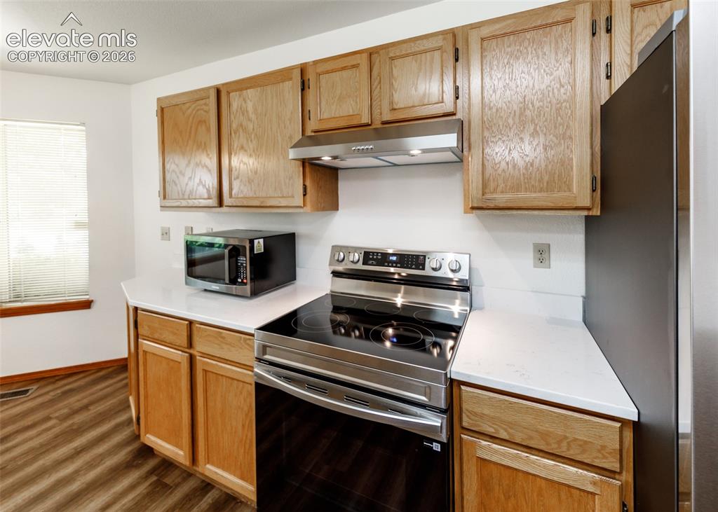 Image 5 of 22: Wood-finish flooring, white countertops, natural wood cabinetry, stainless