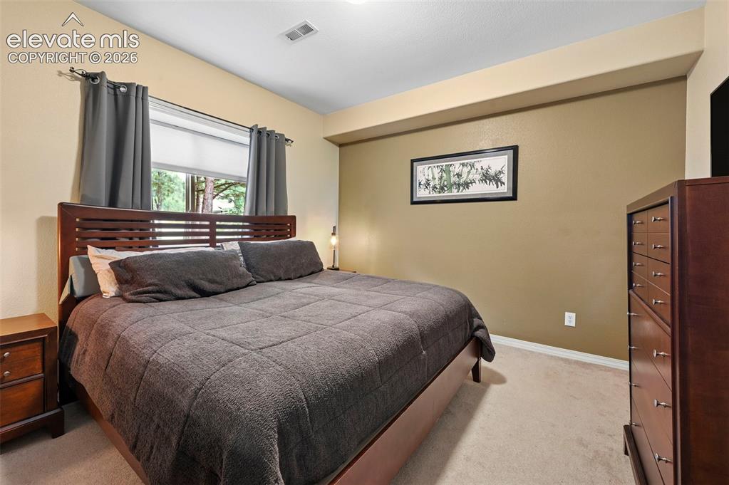 Image 18 of 43: Hardwood bed frame with slat headboard, neutral carpeting, and a built-in c