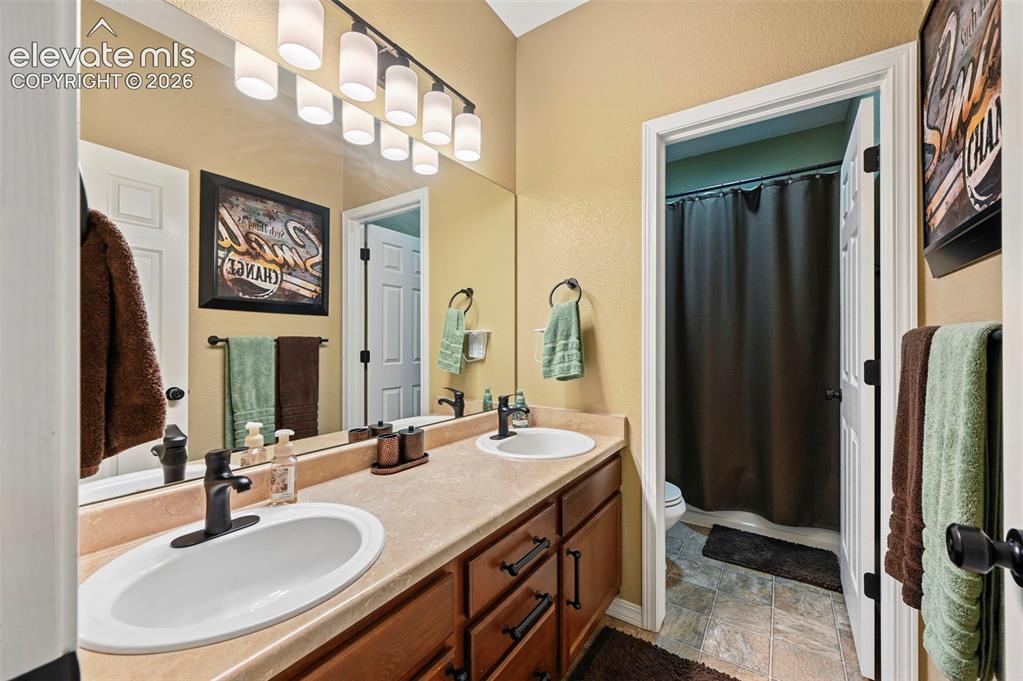 Image 26 of 43: Dual vanity with undermount sinks, wood-finish cabinetry, and matte black f