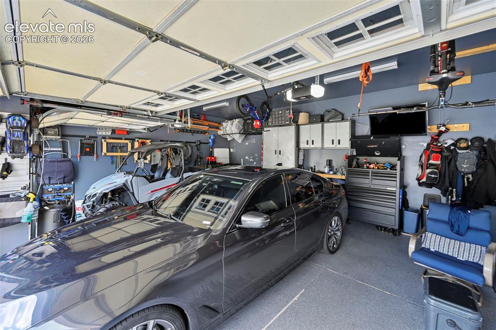 Image 29 of 43: Attached garage with gray epoxy flooring, track lighting, and built-in whit