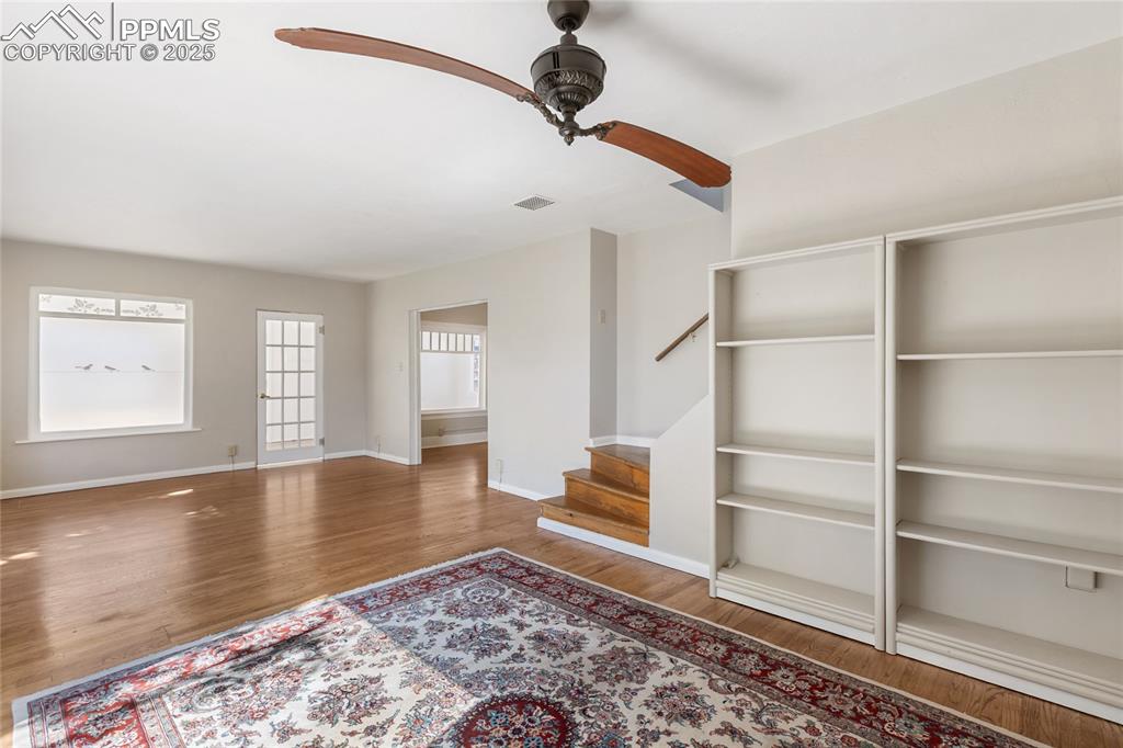 Image 11 of 49: Unfurnished living room with stairway, wood finished floors, and ceiling fa