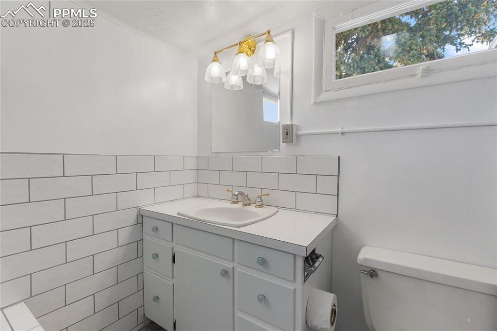 Image 21 of 49: Half bath featuring vanity, tile walls, and crown molding