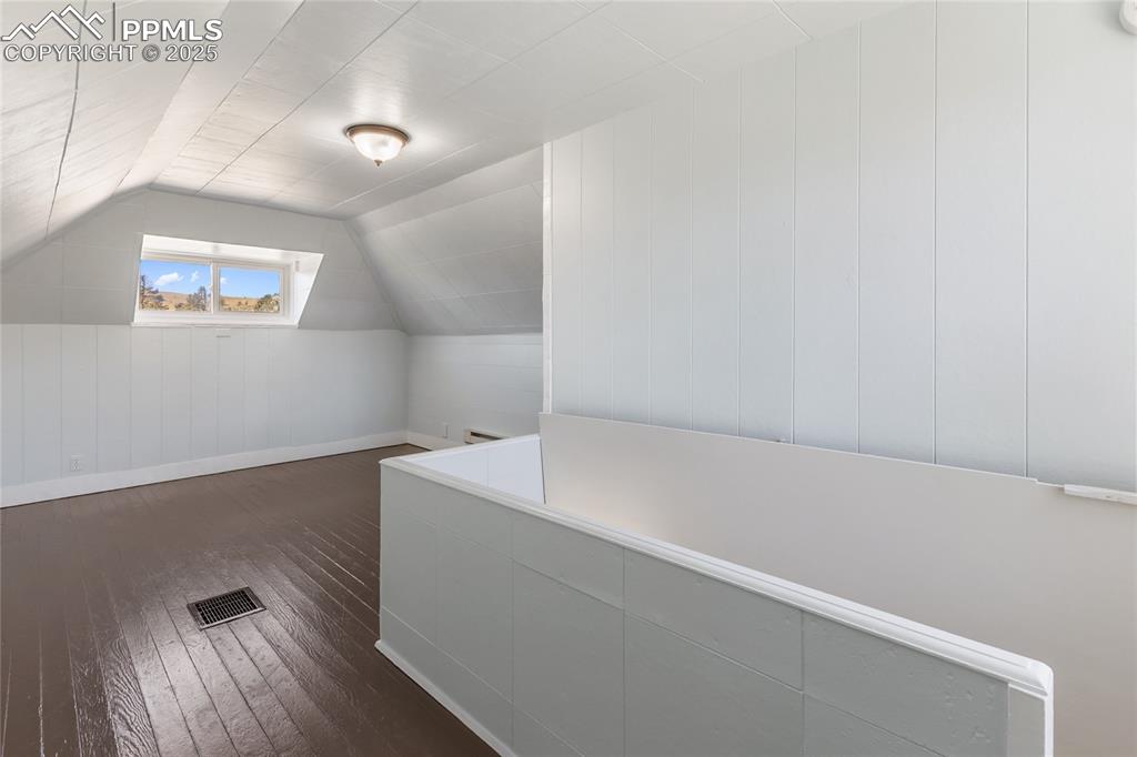 Image 30 of 49: Bonus room with vaulted ceiling, dark wood-type flooring, and wood walls