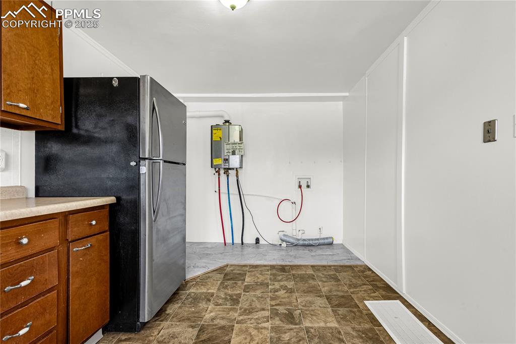 Image 12 of 25: Kitchen featuring freestanding refrigerator, water heater, stone finish flo