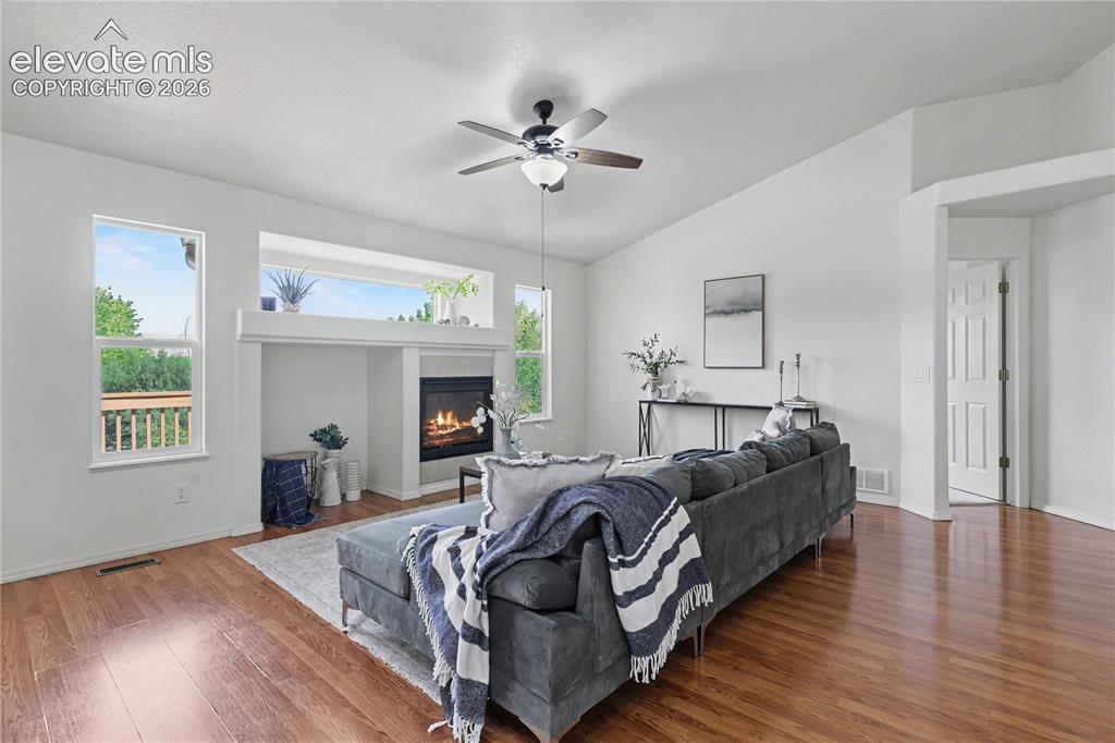 Image 9 of 41: Living area with wood-finish flooring, vaulted ceilings, and a fireplace fe