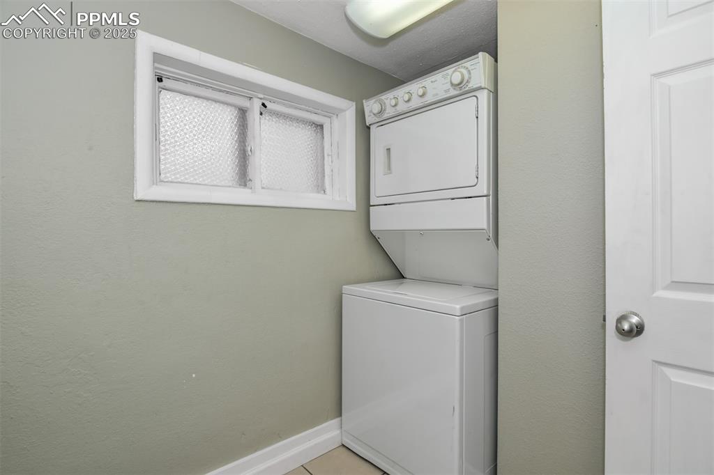 Image 15 of 22: Laundry area with estacked washer and dryer and light tile patterned floors