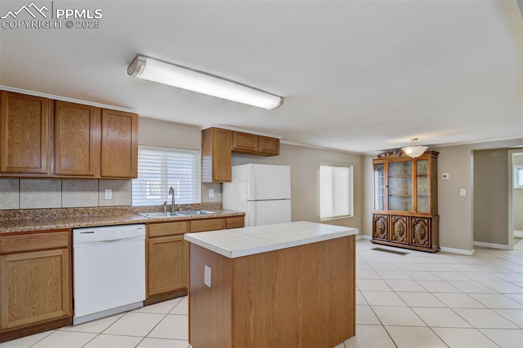 Image 2 of 22: Kitchen with brown cabinetry, light tile patterned floors, white appliances