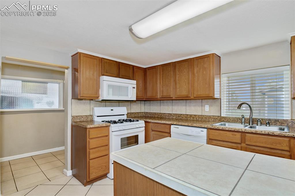 Image 3 of 22: Kitchen featuring white appliances, light tile patterned floors, brown cabi