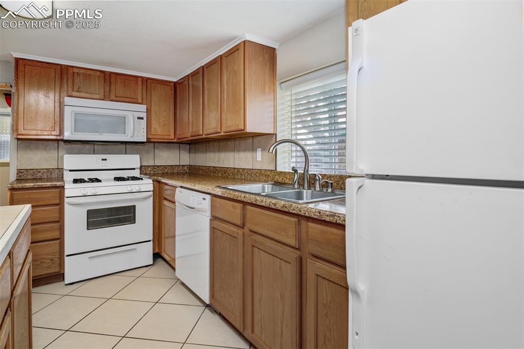 Image 5 of 22: Kitchen with white appliances, light tile patterned floors, and brown cabin