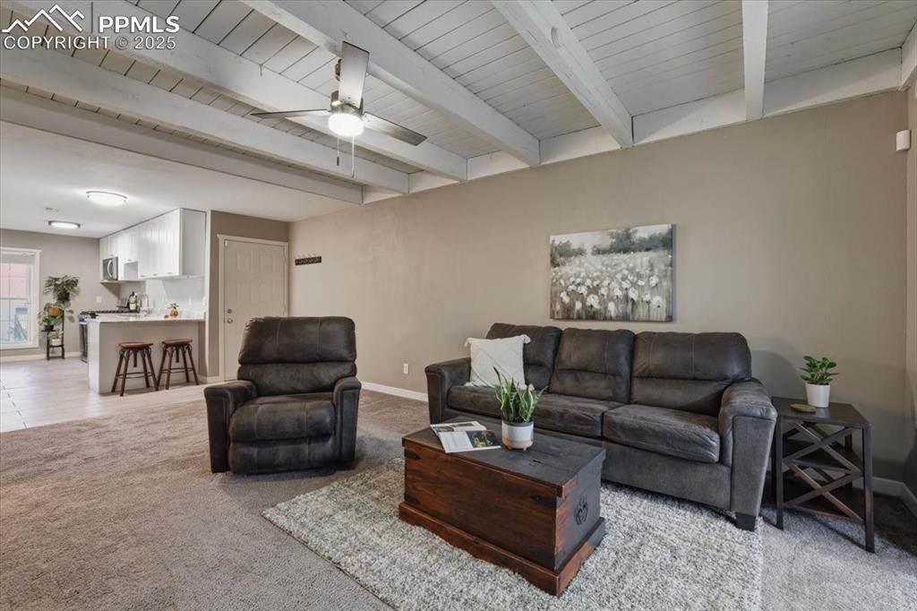 Image 9 of 25: Living room with light carpet, beamed ceiling, and ceiling fan