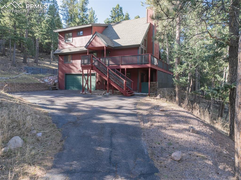 Caption: View of front of home with a wooden deck, driveway, a shingled roof, and an attached garage