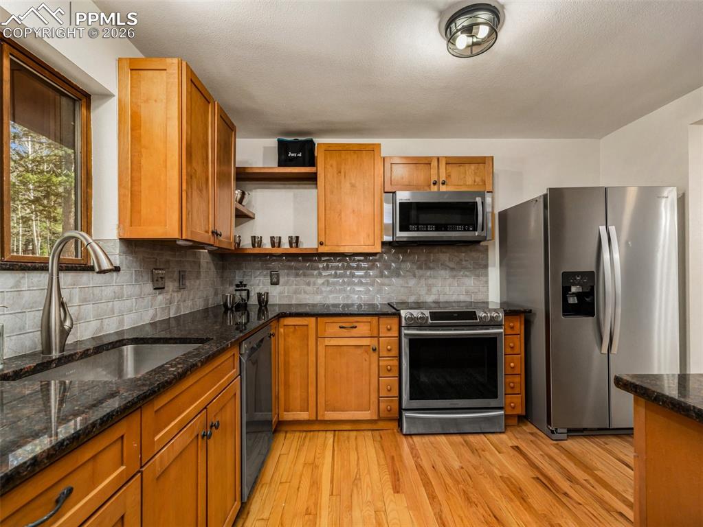 Image 14 of 38: Kitchen with stainless steel appliances, open shelves, dark stone counters,
