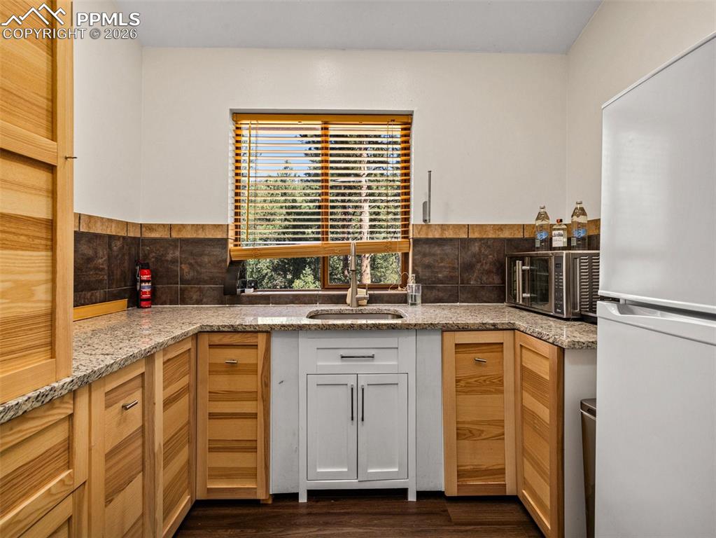 Image 26 of 38: Kitchen featuring freestanding refrigerator, light stone countertops, dark