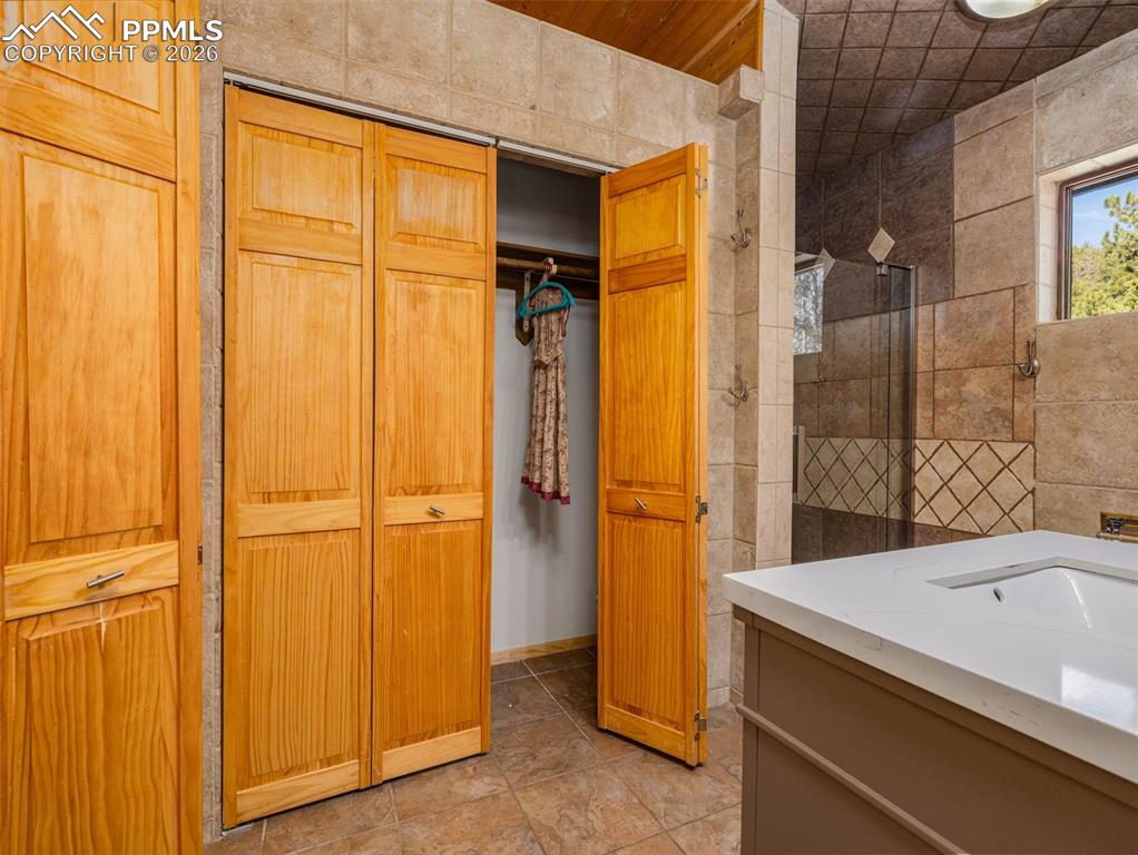 Image 28 of 37: Bathroom with a closet, tile walls, vanity, and a tile shower