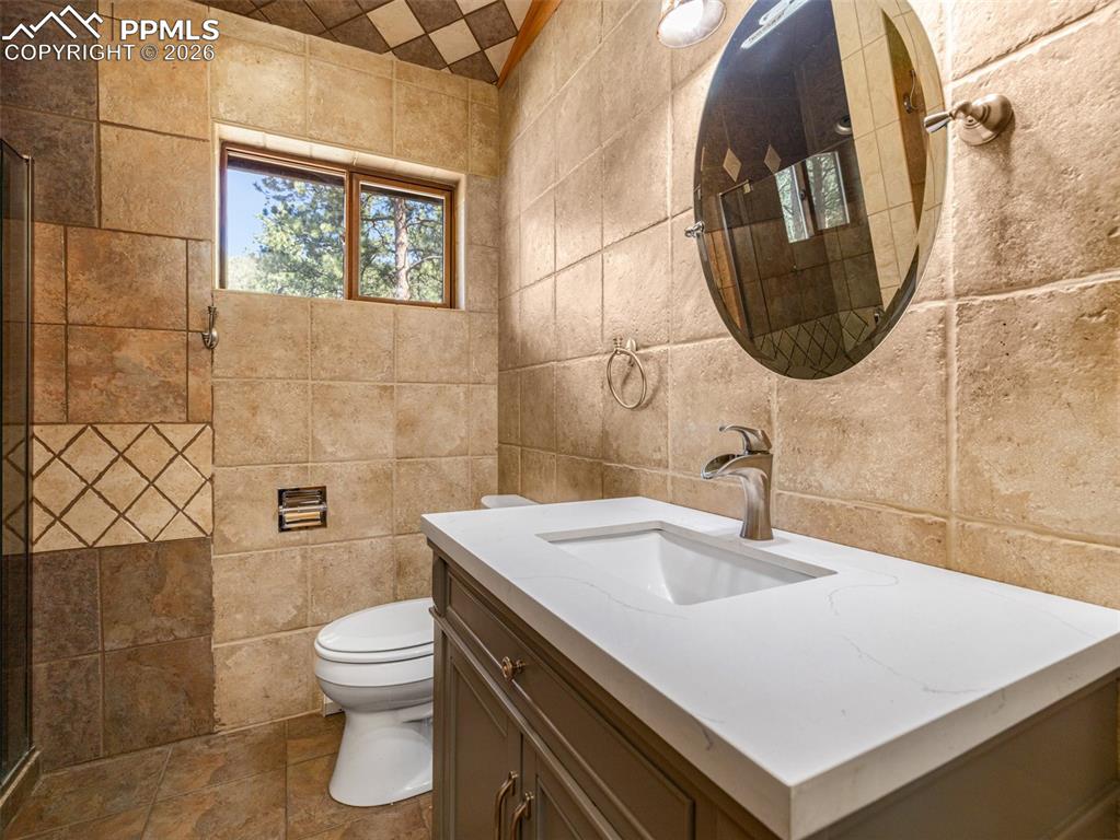 Image 28 of 38: Full bath with vanity, tile walls, and a shower stall