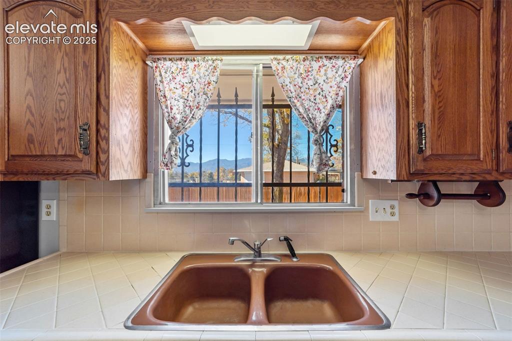 Image 5 of 50: Kitchen sink area featuring a dual basin sink, ceramic tile countertops, li