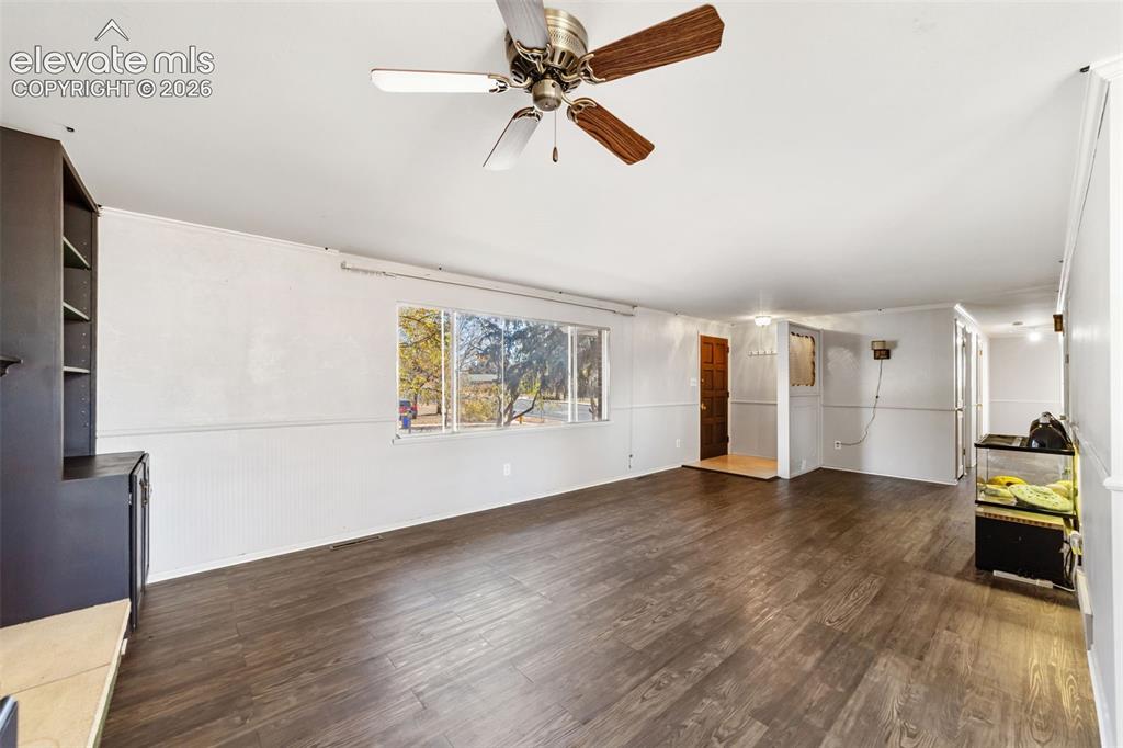 Image 9 of 50: Spacious interior featuring dark wood-finish flooring, a ceiling fan with i