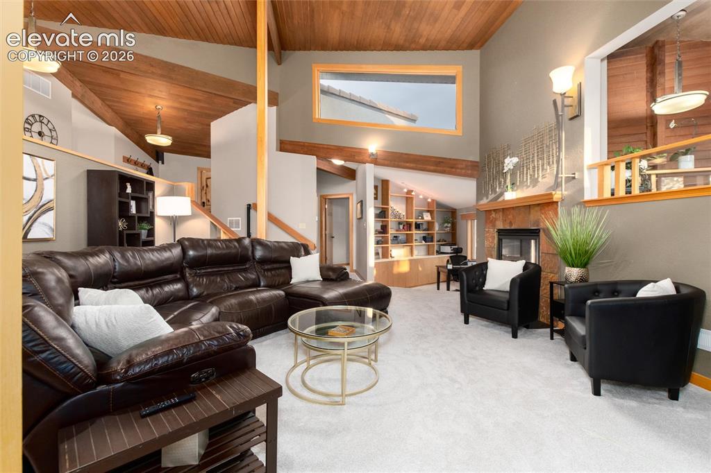 Image 16 of 50: Vaulted ceilings with exposed wood beams, light-toned carpeting, a stone fi