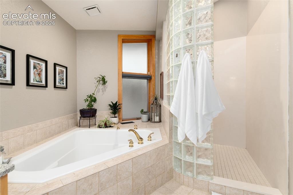 Image 23 of 48: Soaking tub with brass fixtures, surrounded by neutral-toned tiled decking