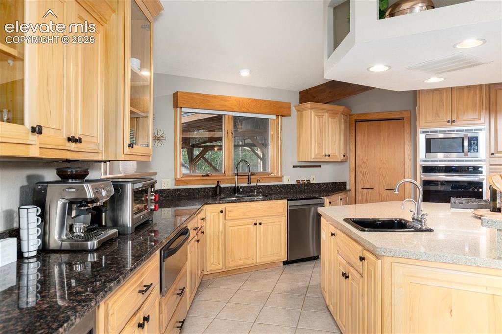 Image 8 of 50: Kitchen featuring light wood cabinetry, dark stone countertops, stainless s