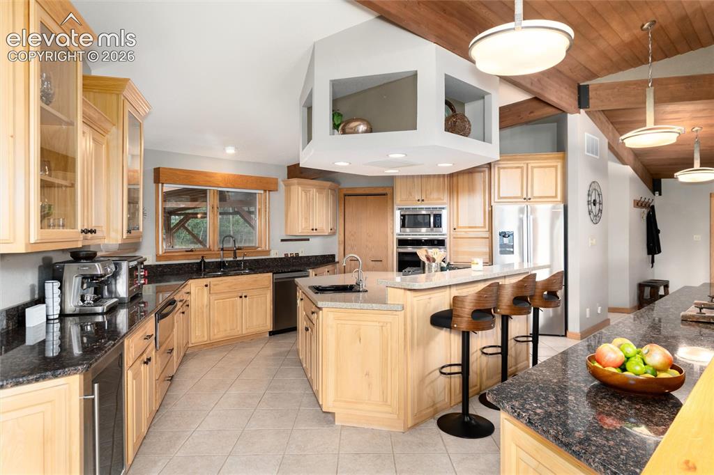 Image 9 of 50: Spacious kitchen featuring light wood cabinetry, dark granite countertops, 