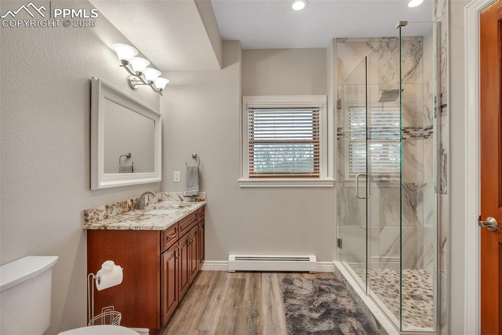 Image 20 of 49: Bathroom featuring a baseboard radiator, vanity, toilet, a shower stall, an
