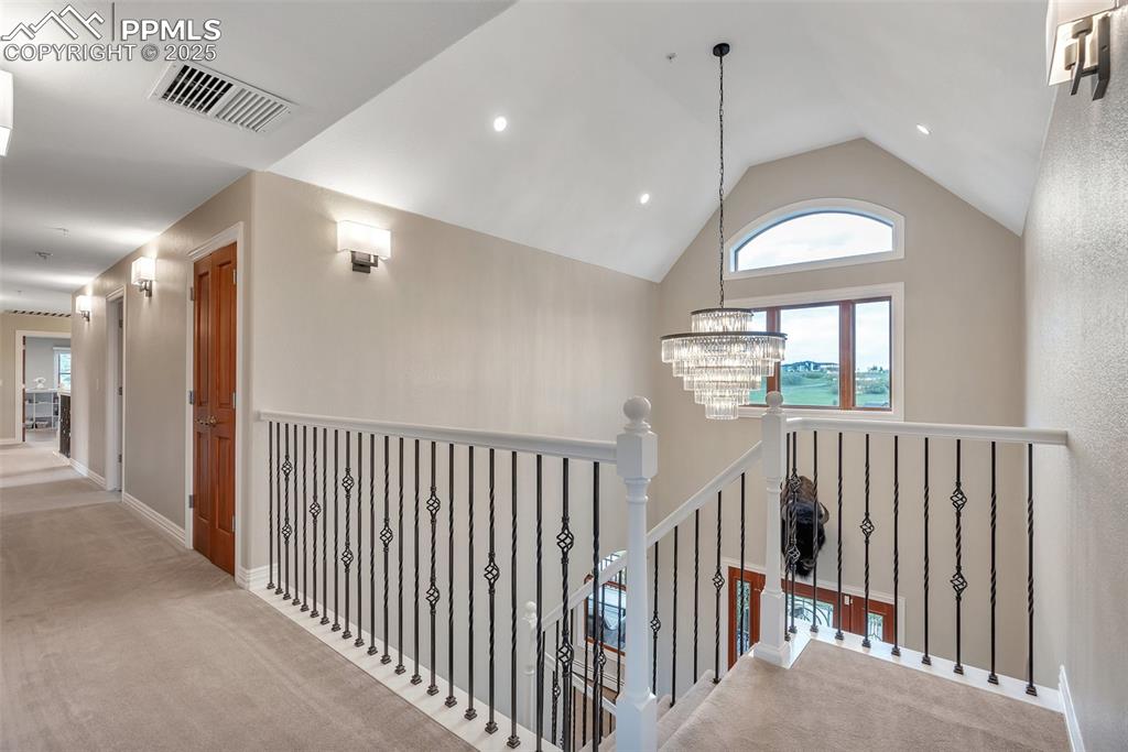Image 21 of 49: Hallway featuring a chandelier, carpet flooring, lofted ceiling, an upstair