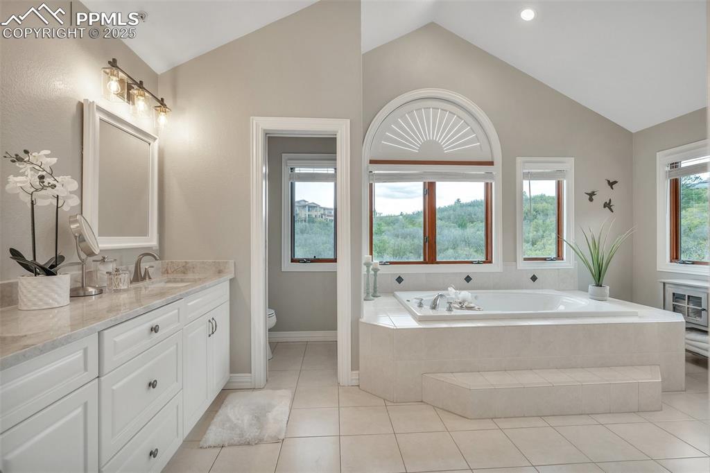 Image 25 of 49: Full bathroom with a garden tub, vanity, toilet, lofted ceiling, and tile p