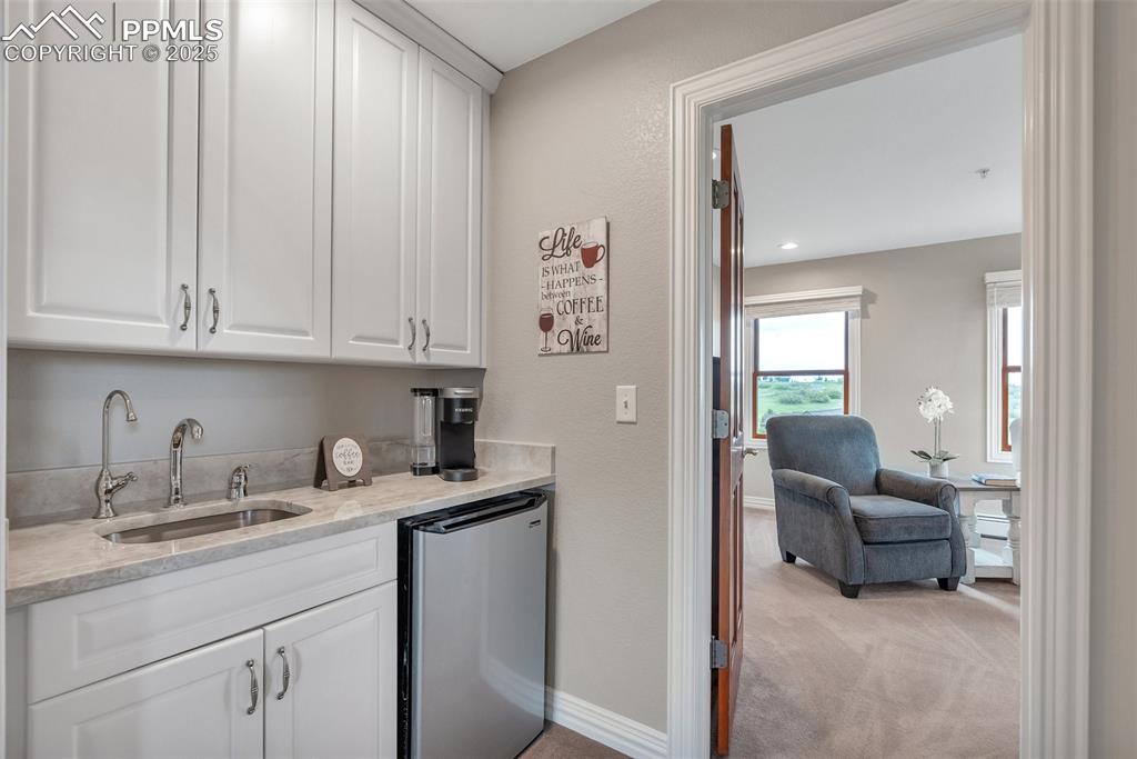Image 27 of 49: Indoor wet bar with fridge, light carpet, and baseboards