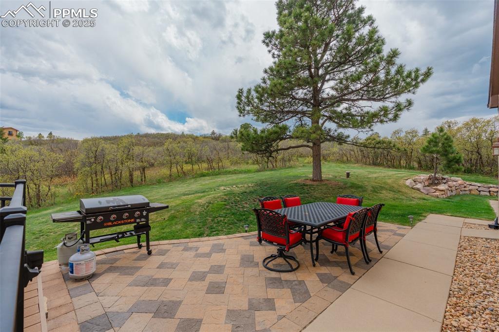 Image 39 of 49: View of patio featuring outdoor dining area, grilling area, and a wooded vi
