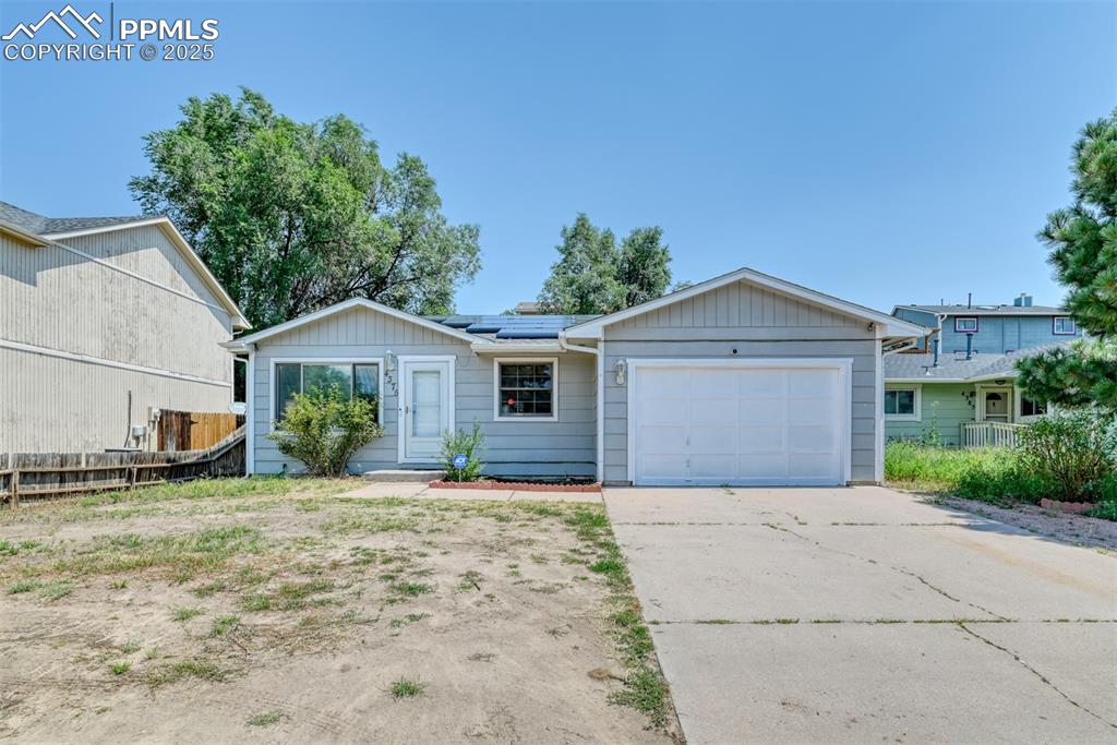 Caption: Ranch-style house with roof mounted solar panels, an attached garage, and driveway