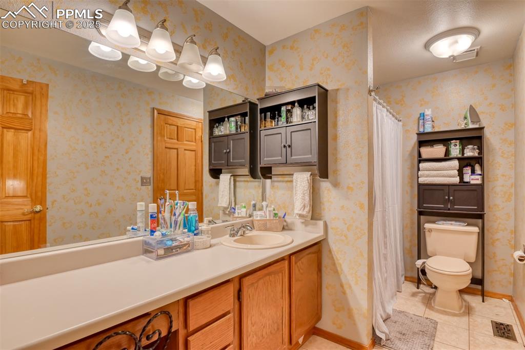 Image 15 of 32: Full bath with wallpapered walls, vanity, tile patterned flooring, and a sh