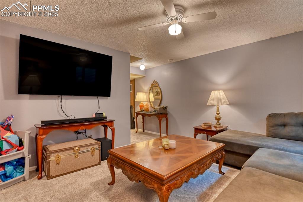 Image 23 of 32: Living area featuring carpet flooring, a textured ceiling, and ceiling fan