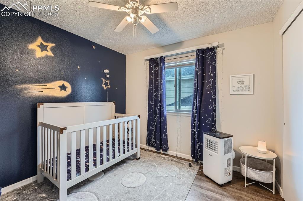 Image 15 of 28: Bedroom with a textured ceiling, wood finished floors, a crib, and ceiling 