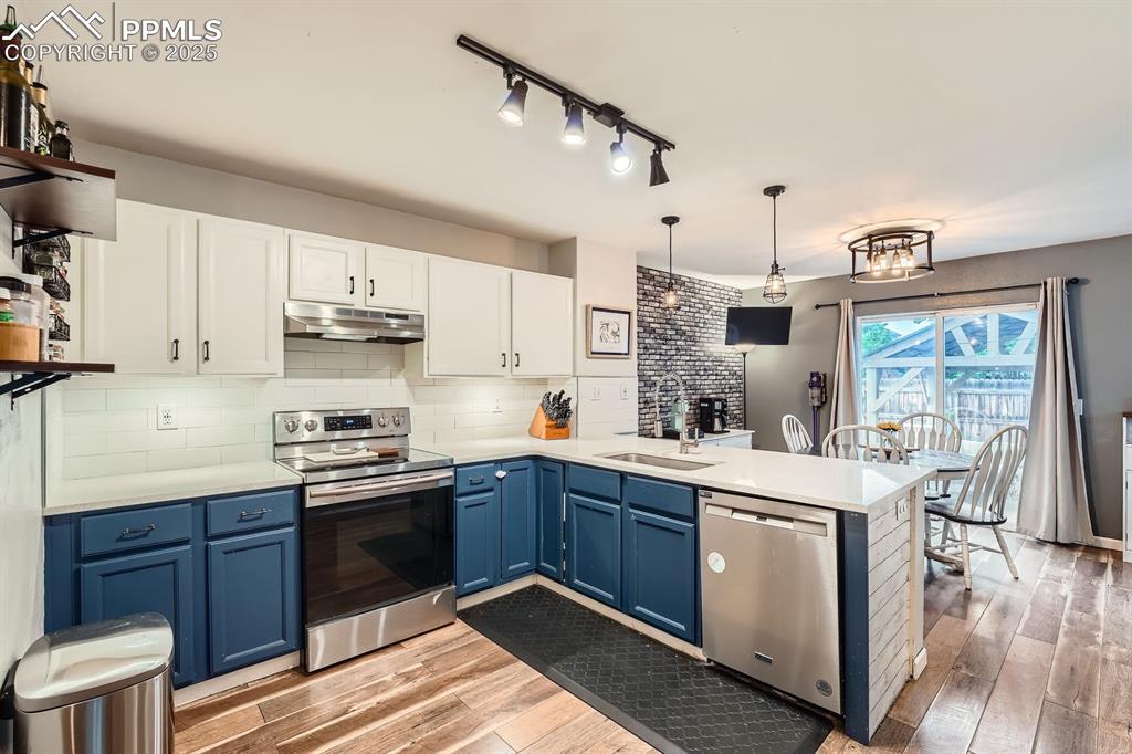 Image 8 of 28: Kitchen with a peninsula, open shelves, blue cabinetry, and appliances with