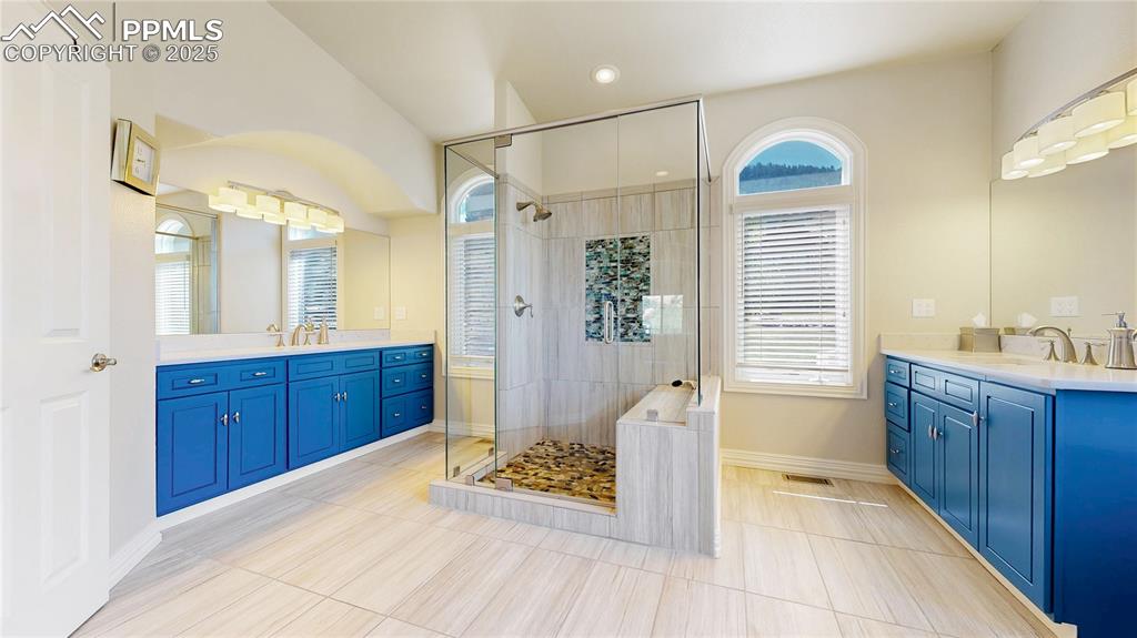 Image 16 of 46: Full bath featuring two vanities, a shower stall, and light tile patterned 