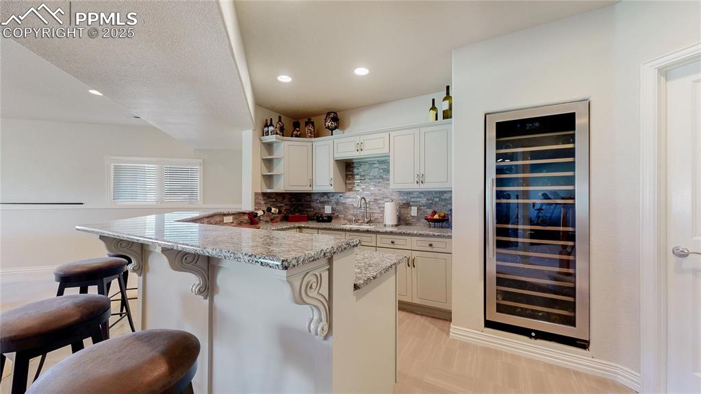 Image 23 of 46: Kitchen with wine cooler, decorative backsplash, light stone countertops, a