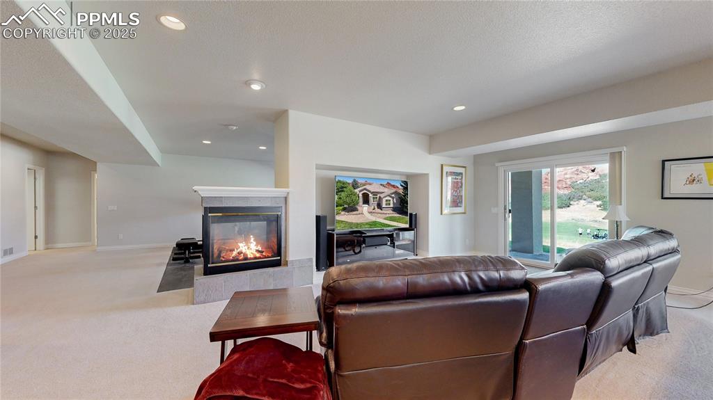 Image 25 of 46: Living area with light colored carpet, recessed lighting, and a tiled firep