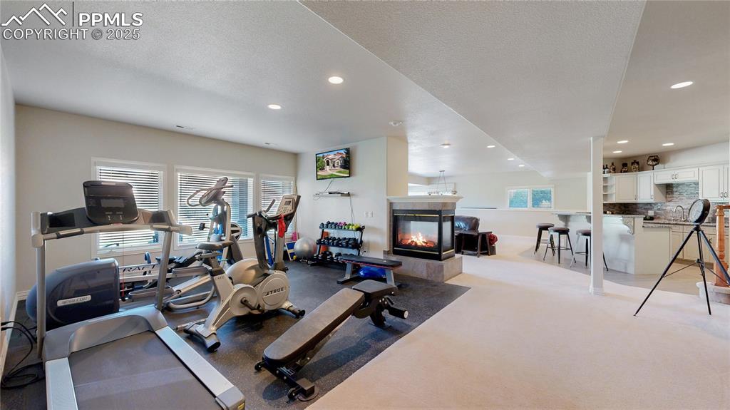 Image 27 of 46: Workout room featuring a tiled fireplace, recessed lighting, light carpet, 