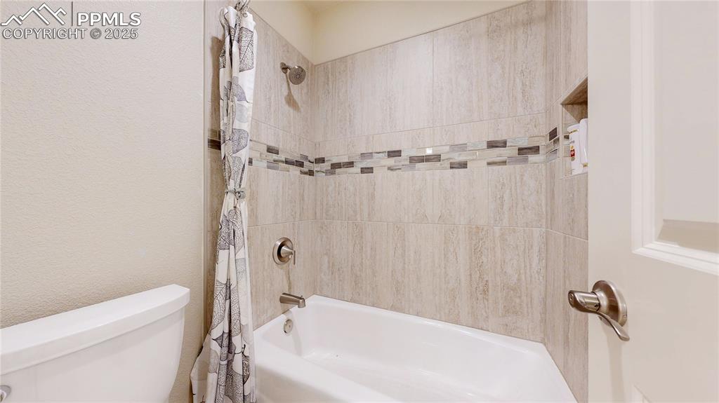 Image 30 of 46: Bathroom featuring shower / bath combination with curtain and a textured wa