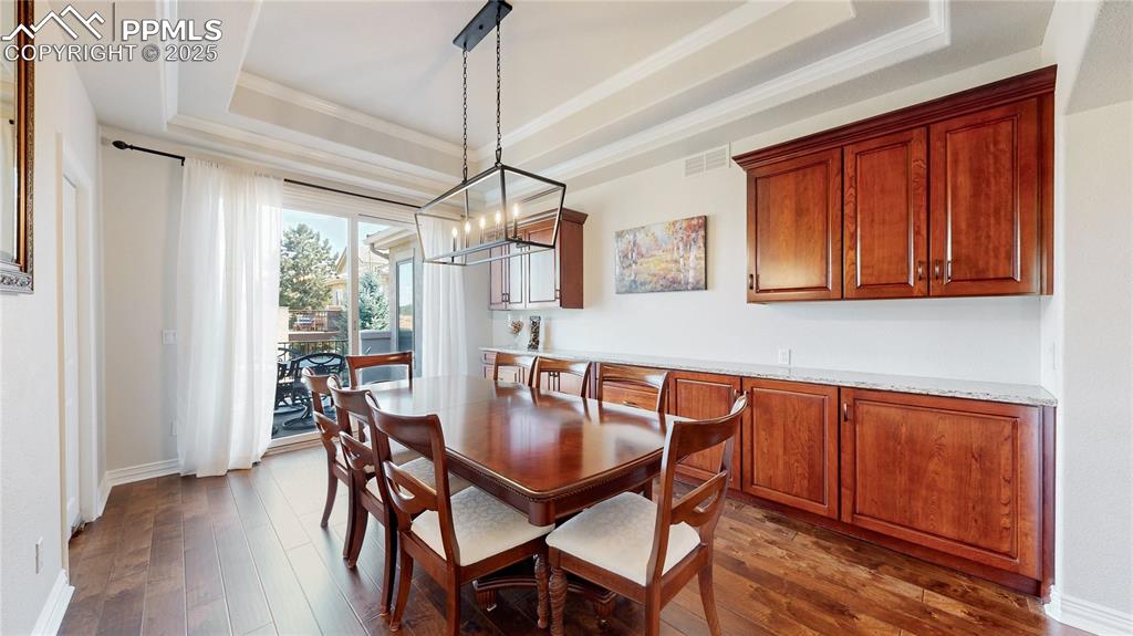 Image 8 of 46: Dining room featuring a tray ceiling, a chandelier, dark wood-style floorin